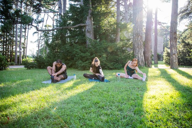 Foto tres personas deportivas en un parque público durante un entrenamiento se están estirando