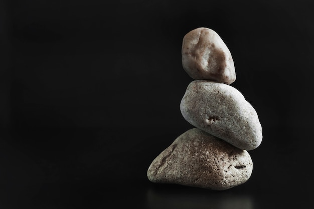 Tres piedras se colocan una encima de la otra manteniendo el equilibrio. Fondo oscuro. Copie el espacio ..