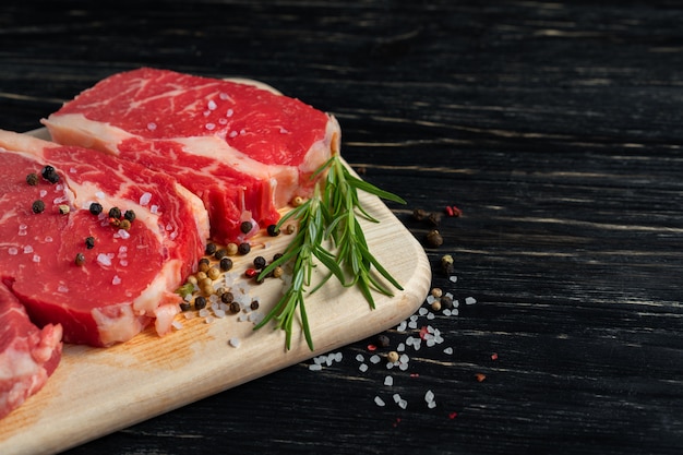 Tres piezas de jugosa carne cruda en una tabla de cortar sobre una mesa de madera negra