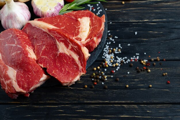 Tres piezas de jugosa carne cruda con verduras en una tabla para cortar piedra