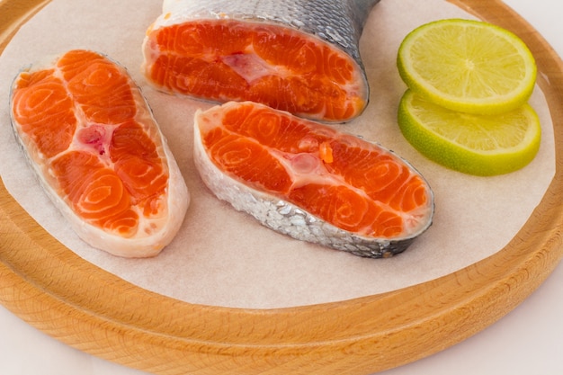 Tres piezas de salmón crudo y dos rodajas de limón en la tabla de cortar.