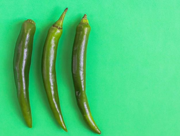 Três pimentas verdes quentes estão à esquerda sobre um fundo verde