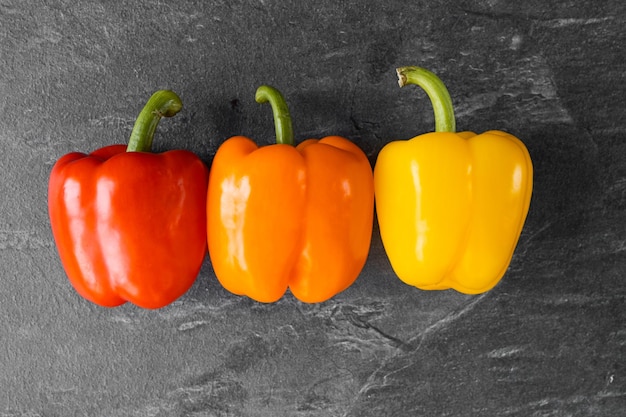 Tres pimientos sobre verduras de fondo oscuro para las verduras del restaurante sobre un fondo blanco