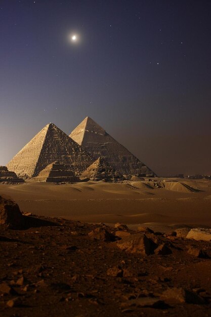 Foto três pirâmides no deserto à noite.