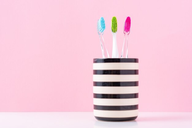 Tres plásticos coloridos cepillos de dientes en vidrio sobre un fondo rosa, de cerca