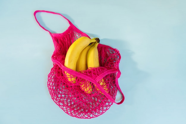 Tres plátanos maduros amarillos en una bolsa de hilo de algodón ecológico fucsia