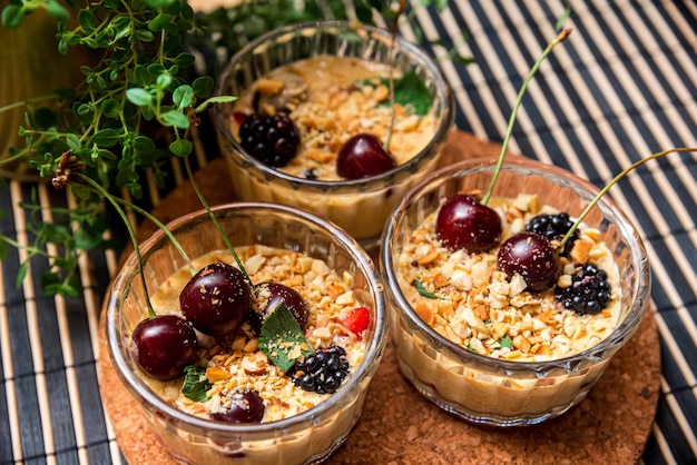 Três porções de sobremesa de creme de baunilha com amendoim triturado e amoras e cerejas frescas