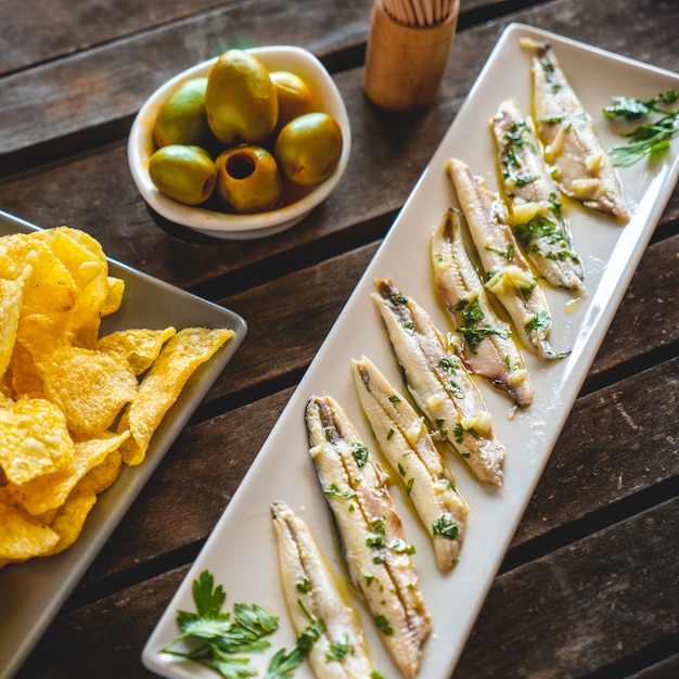 Três pratos com batatas fritas, anchovas colhidas e azeitonas verdes em uma mesa de madeira escura com palitos de dente. petiscos típicos espanhóis.