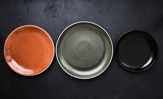 Três pratos vazios multicoloridos em fundo preto em closeup
