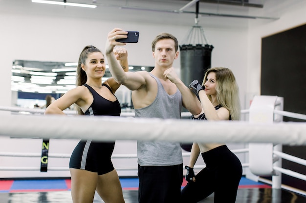 Três pugilistas profissionais e instrutores de fitness estão fazendo selfie em pé no meio do ringue de boxe