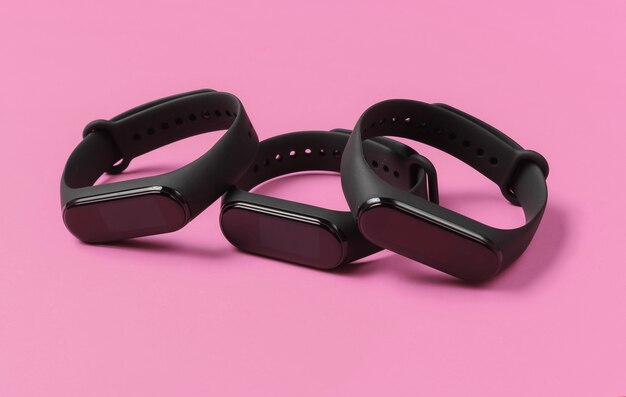 Três pulseiras inteligentes em fundo rosa. Gadgets modernos para esportes e atividades cotidianas