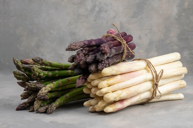 Tres racimos de espárragos frescos diferentes aislados en gris. Espárragos morados, blancos y verdes. Vegetales frescos.