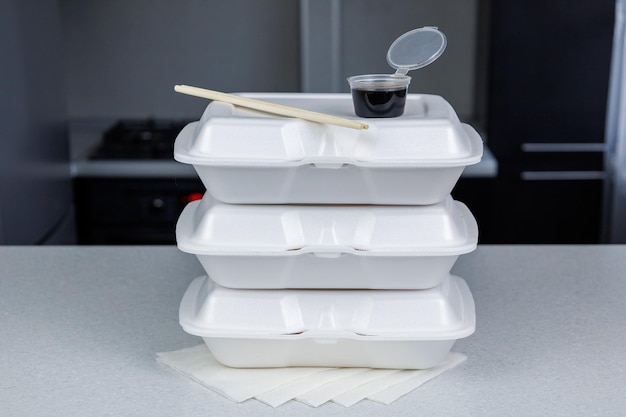 Três recipientes de comida branca estão na mesa da cozinha Pauzinhos para comer sushi e uma caixa de molho de soja