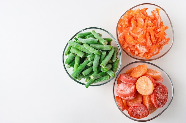 Três recipientes de vidro com vegetais congelados em um fundo claro