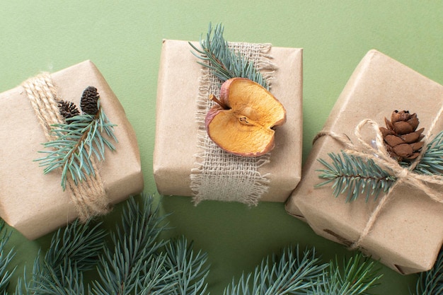 Tres regalos de Navidad envueltos en papel kraft y pintados con materiales naturales sobre un fondo verde