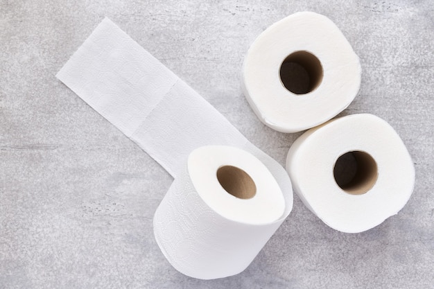 Tres rollos de papel higiénico blanco sobre un fondo de hormigón gris, profundidad de campo