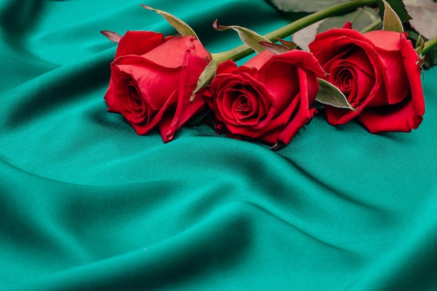 Foto três rosas sobre uma seda verde