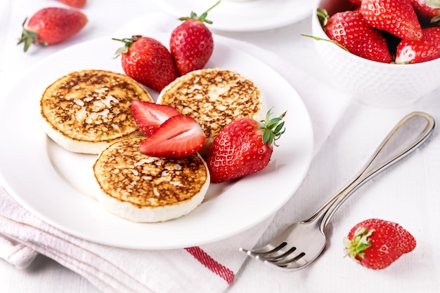 Tres sabrosos panqueques caseros de requesón con fresas en plato blanco