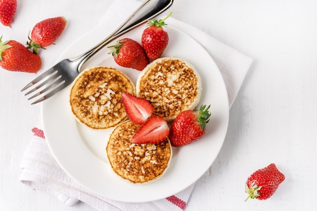 Tres sabrosos panqueques caseros de requesón con fresas en plato blanco