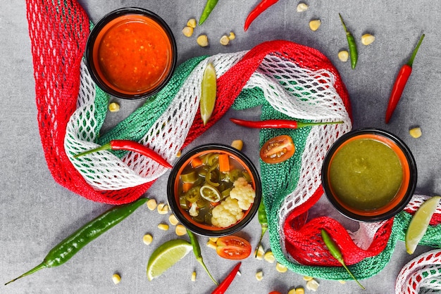 Tres salsas mexicanas con verduras y bandera mexicana sobre fondo gris