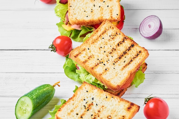 Três sanduíches com presunto, alface e legumes frescos em um fundo branco