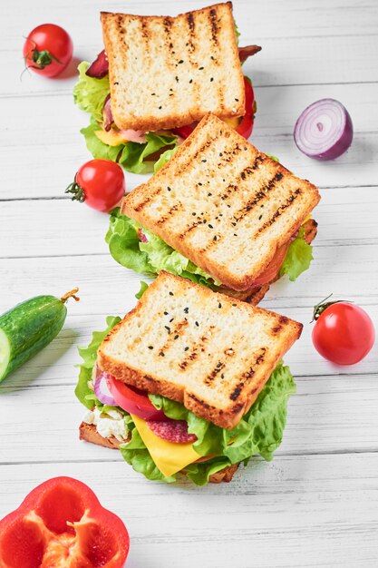 Tres sándwiches con jamón, lechuga y verduras frescas sobre un fondo blanco