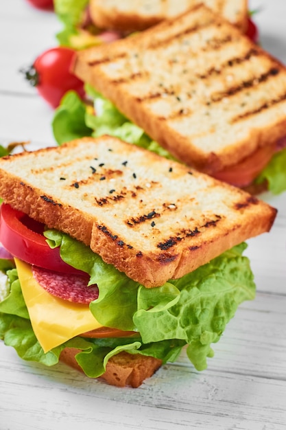 Tres sándwiches con jamón, lechuga y verduras frescas sobre un fondo blanco