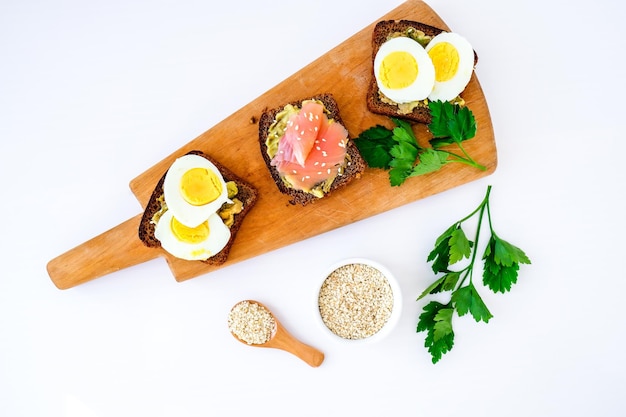 Tres sándwiches en tabla de cortar. Tostadas de guacamole con huevos y salmón. Comida saludable vegetariana. Alimentación saludable. Dieta