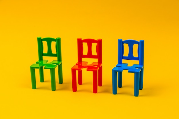 Tres sillas de juguete de plástico de diferentes colores sobre fondo amarillo.