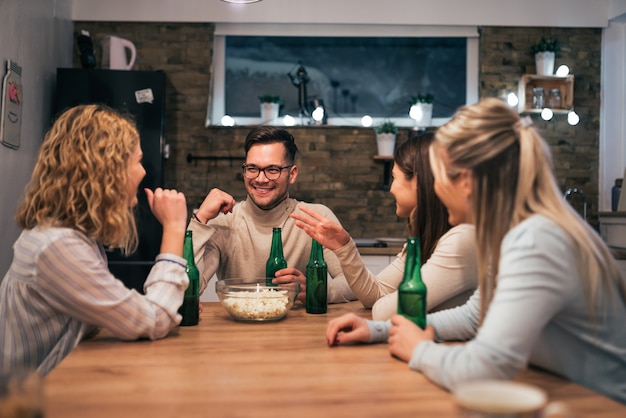 Tres sonrientes y un amigo masculino sentado alrededor de la mesa en casa por la noche.