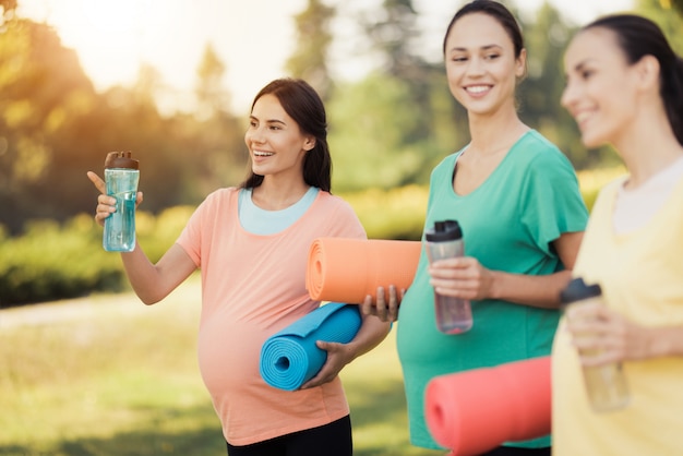 Tres sonrientes chicas embarazadas con colchonetas de yoga.