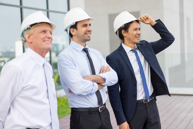 tres sonrientes empresarios diversos mirando hacia otro lado, con cascos y de pie