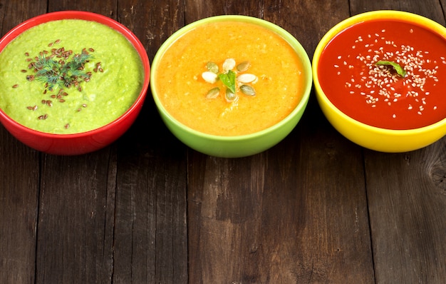 Foto três sopas de legumes coloridos frescos - tomate, abóbora e ervilhas verdes em uma mesa de madeira fechar