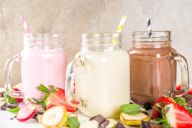 Tres tarros de albañil con batidos o batidos. Verano saludable desayuno, almuerzo bebidas - batidos de plátano, chocolate y fresa