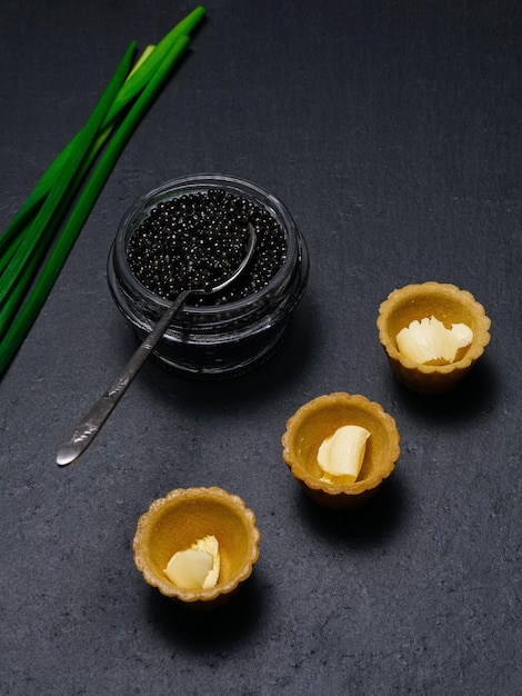 Tres tartaletas de caviar negro con plumas de cebolla verde mantequilla en un plato de pizarra de la cocina rusa