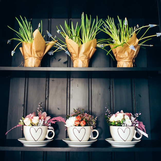 Tres tazas blancas con flores en el estante.