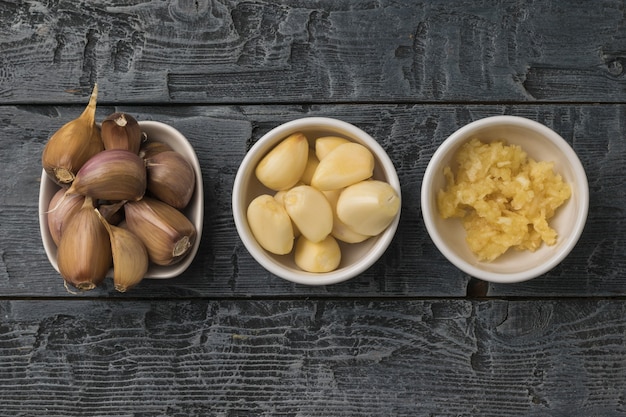 Tres tazones de ajo entero y procesado sobre una mesa de madera. Una especia popular para la cocina.