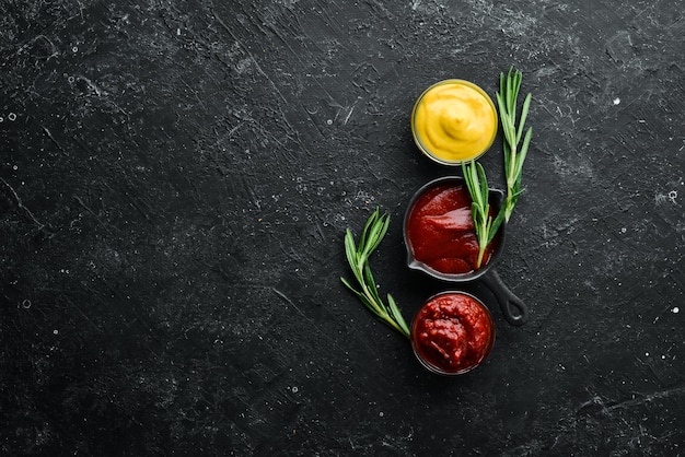 Tres tazones de salsas: salsa barbacoa, ketchup y mostaza. Sobre un fondo de piedra negra. Vista superior.