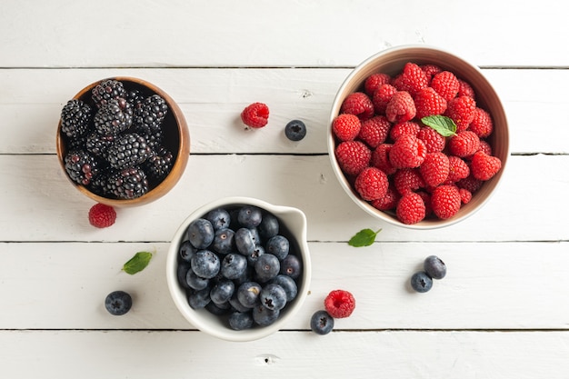 Três tigelas com frutos silvestres, framboesa, mirtilos, amoras, vista do zênite