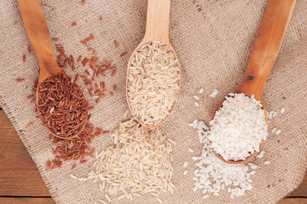 Tres tipos de arroz en cuchara de madera arroz marrón, rojo y redondo sobre fondo de madera