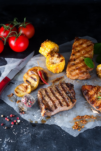 Tres tipos de carnes a la brasa con verduras y especias sobre papel.