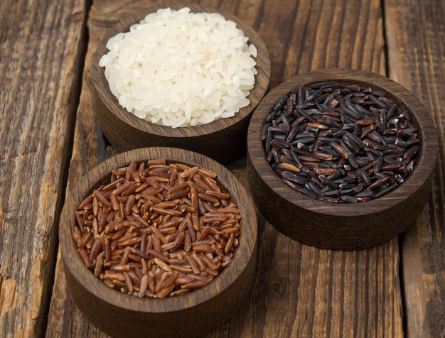 Três tipos de arroz em tigelas de madeira em uma velha mesa de madeira vermelho preto e branco cópia espaço