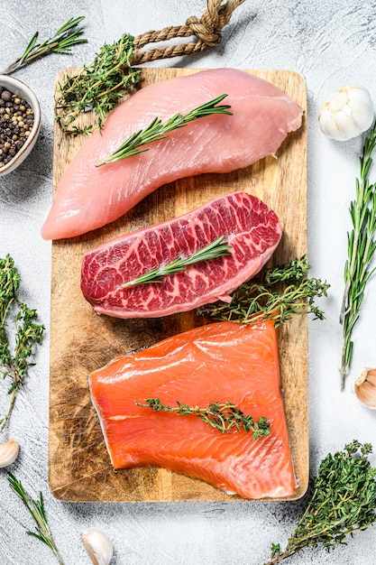 Foto três tipos de bifes. lâmina superior de carne, filé de salmão e peito de peru. peixe orgânico, aves e carnes bovinas. plano de fundo cinza. vista do topo.