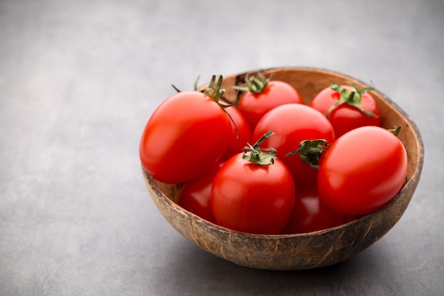 Três tomates cereja em uma tigela de madeira em um cinza.