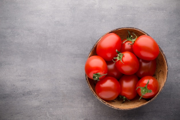 Três tomates cereja em uma tigela de madeira em um cinza.