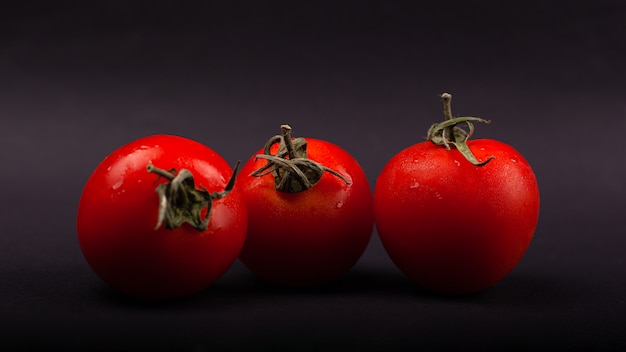 Três tomates de cereja suculentos pequenos vermelhos em um close-up preto do fundo.