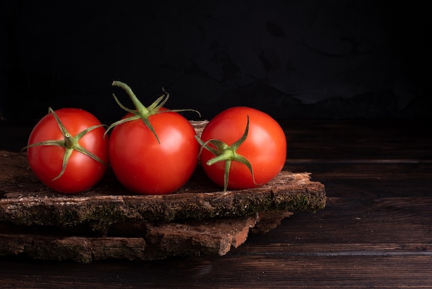 Tres tomates frescos rojos sobre una mesa de madera.