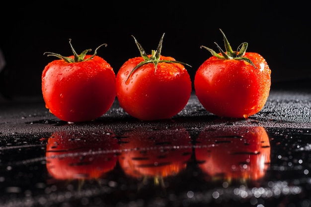 Tres tomates frescos sobre un fondo negro gotas de agua