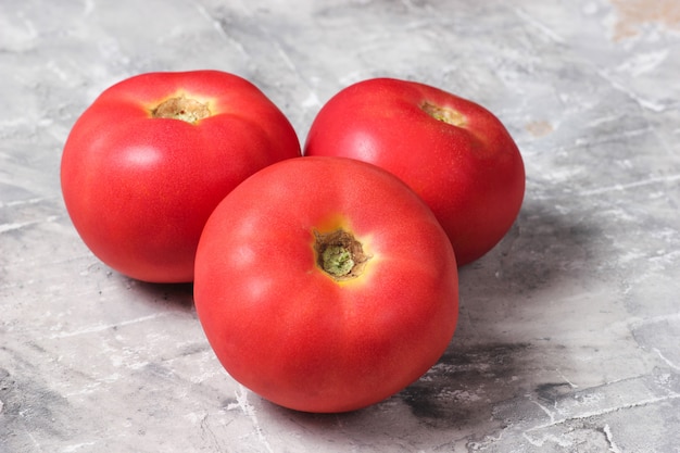 Três tomates maduros em uma mesa de concreto cinza
