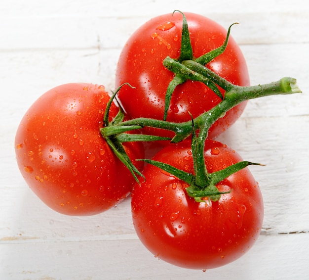 Três tomates na mesa de madeira branca